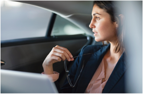 A businesswoman looking out of a car window with a laptop beside her